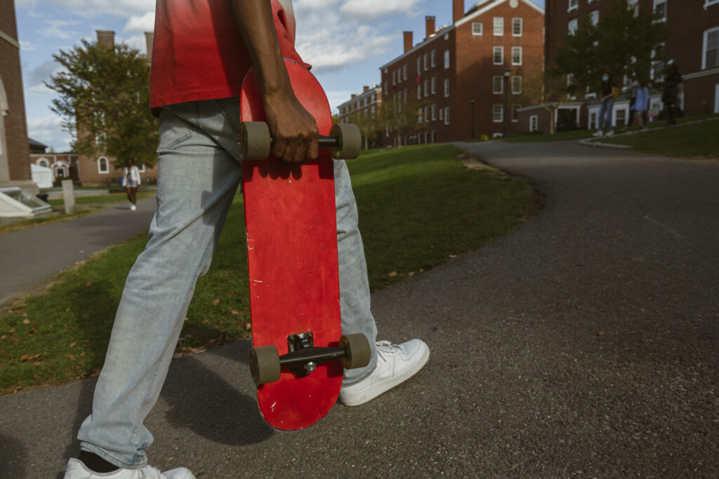 Student walks with red skateboard in hand.