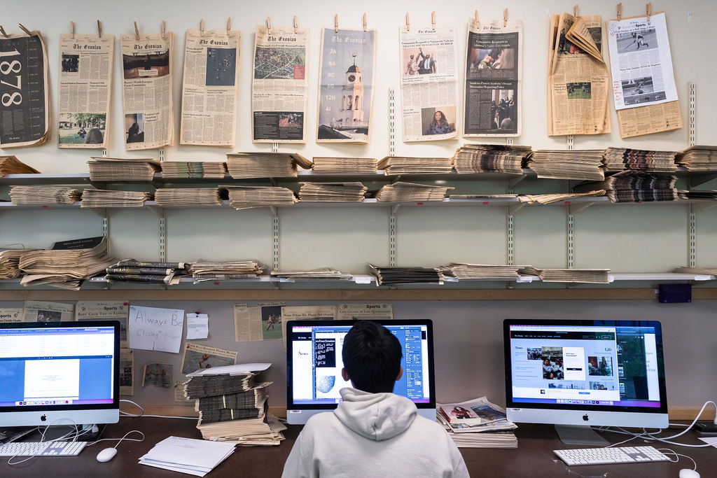 Student looks at computer with newspapers hung around them.