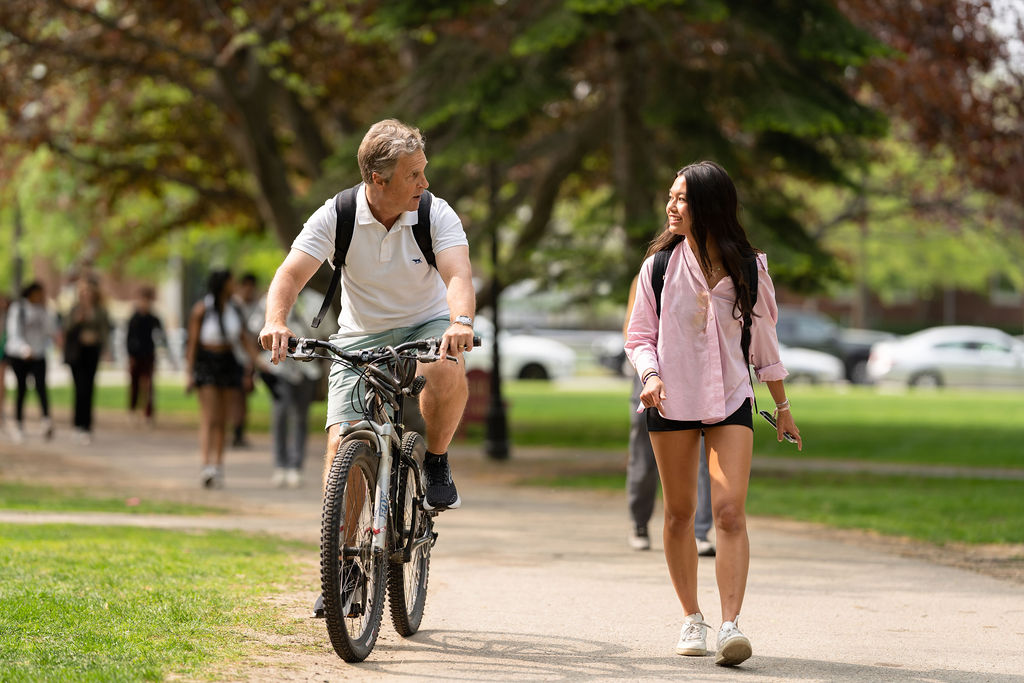 Teacher on a bike rides along with student walking.