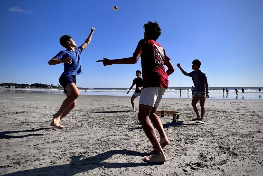 Group of students play spike ball on beach.