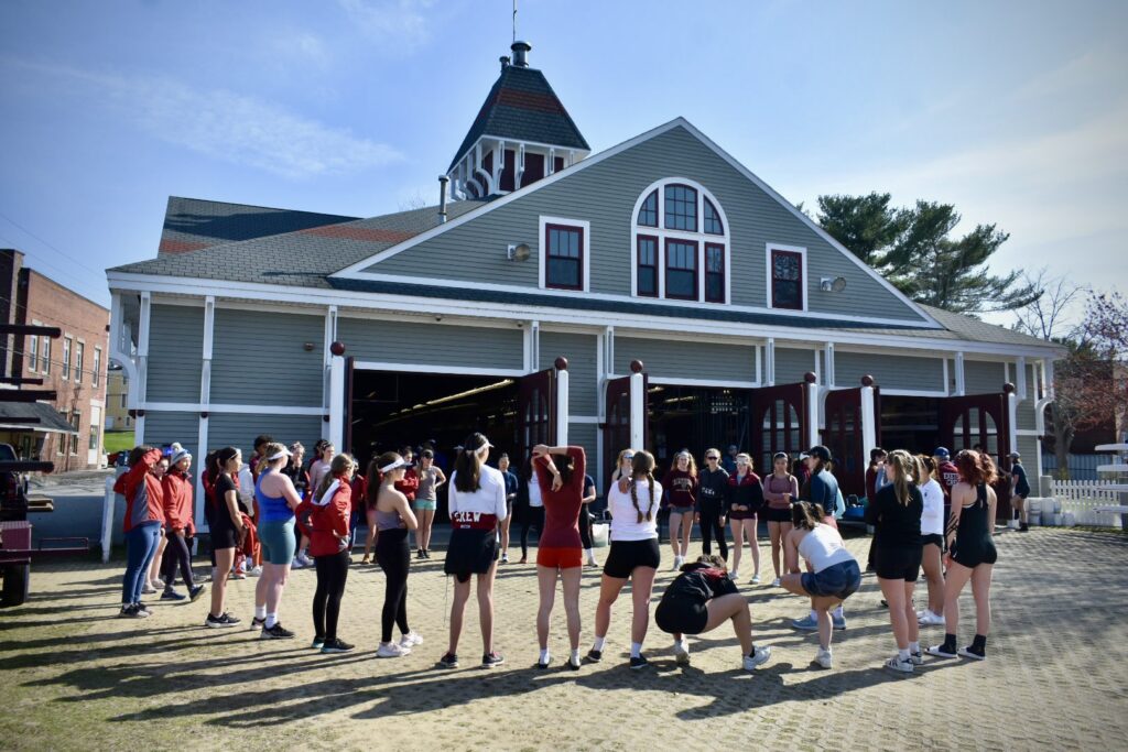 Group of students stand around boat house.