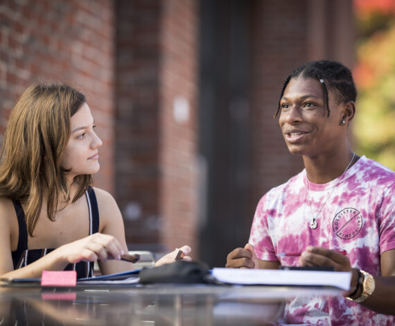 Students sit together at an outdoor table looking at text books