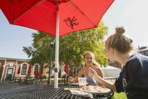 Students sit at outside table under red umbrella eating lunch