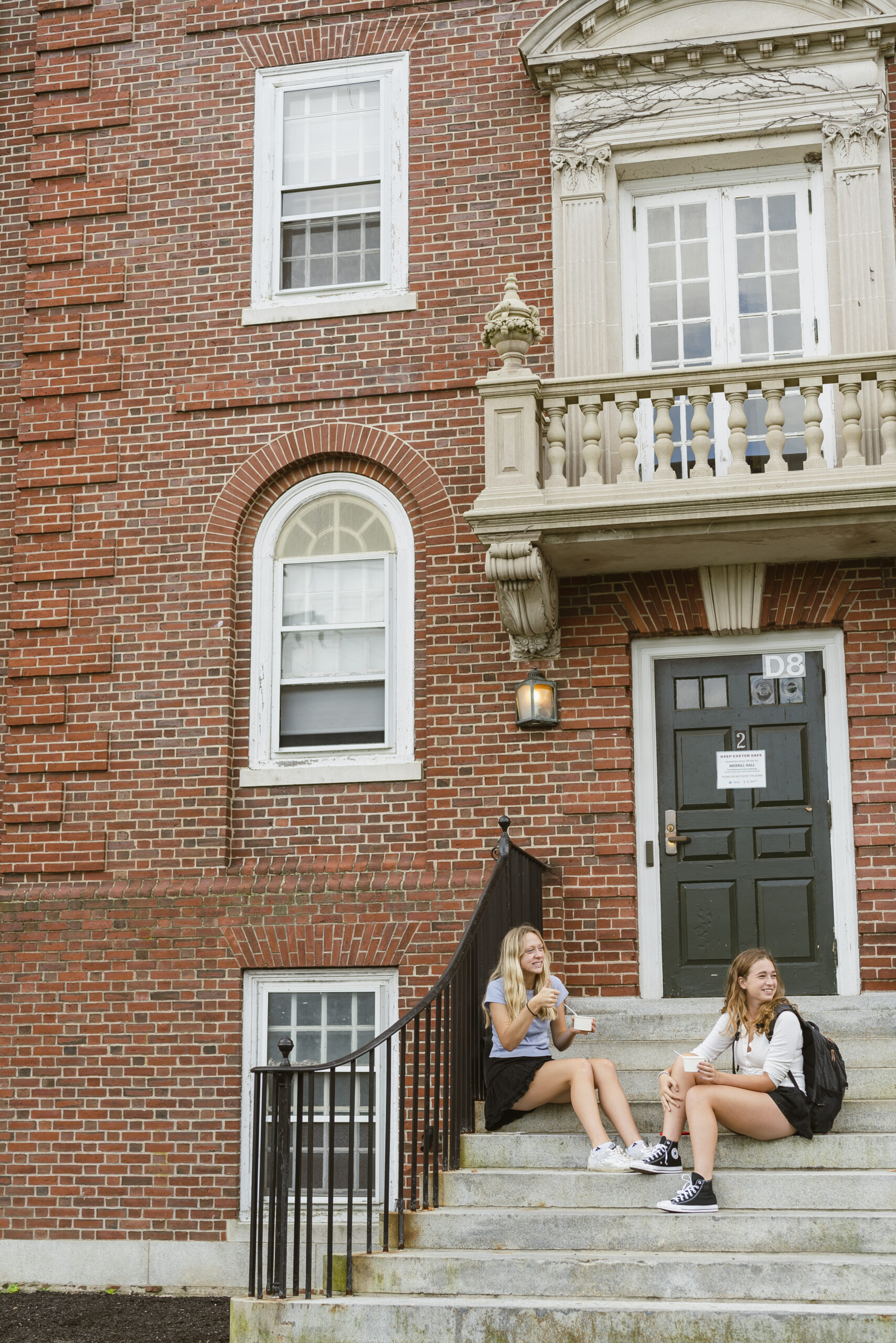 Two girls sit on concrete stairs in front of dorm