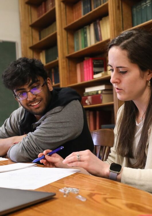 Teacher sits with student reviewing papers