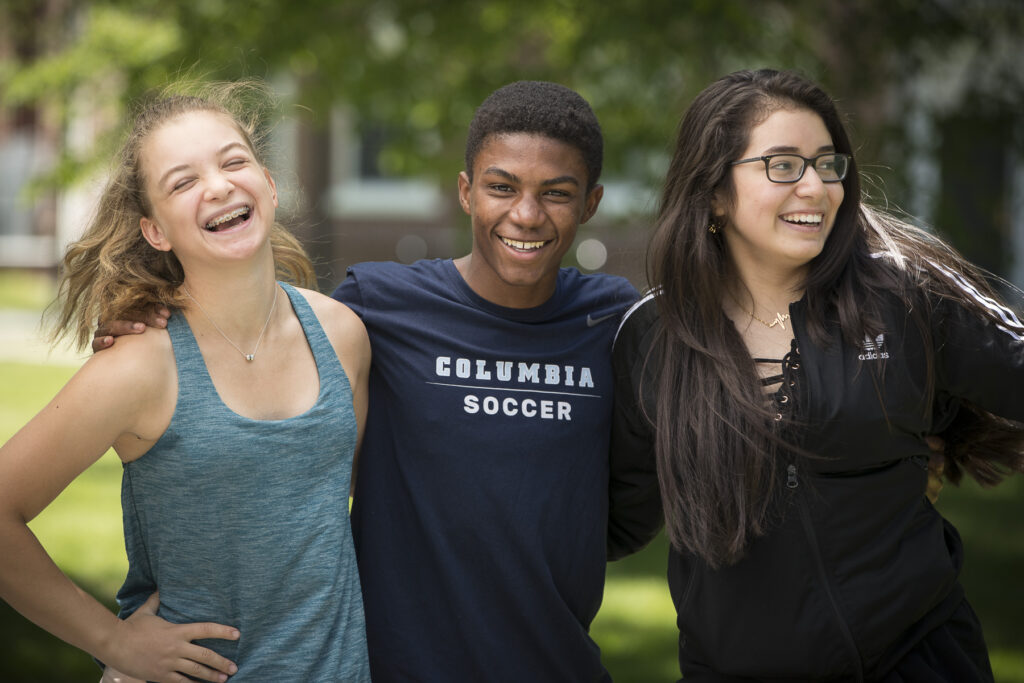 Three students stand together and smile on green lawn