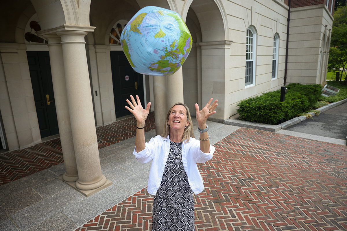 Patty Burke Hickey throws inflatable globe in the air standing in front of Phillips Hall