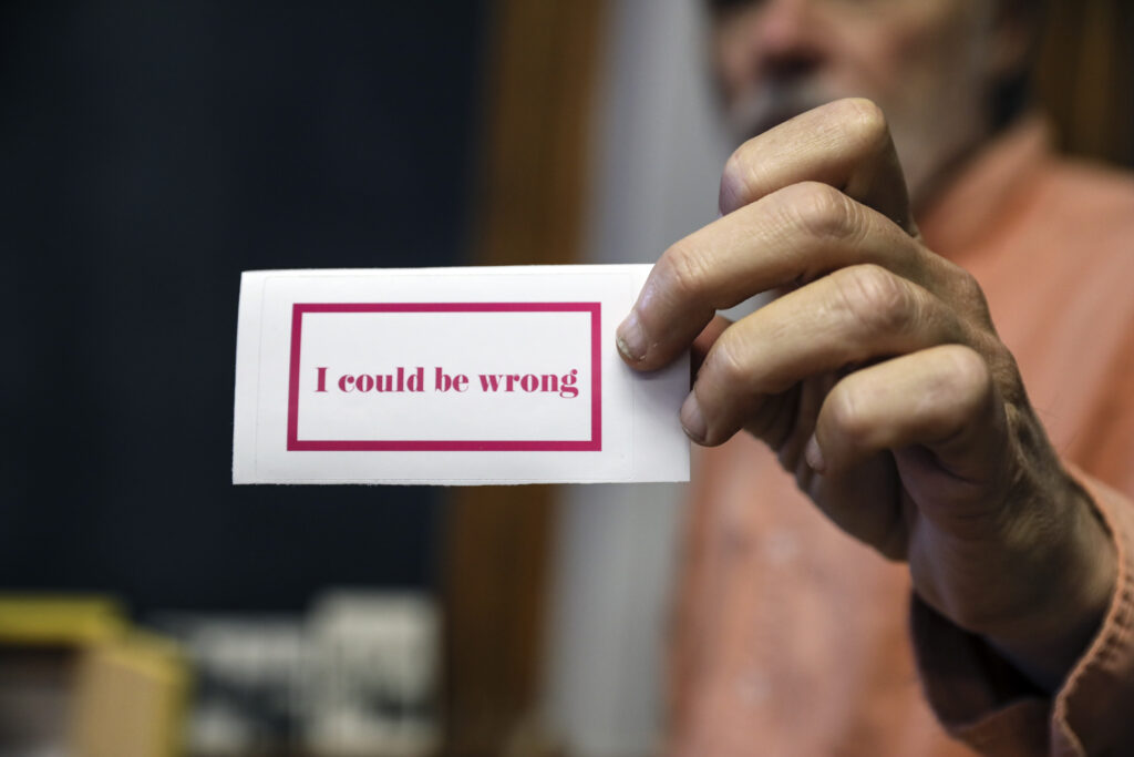 Teacher holds sticker that reads "I could be wrong"