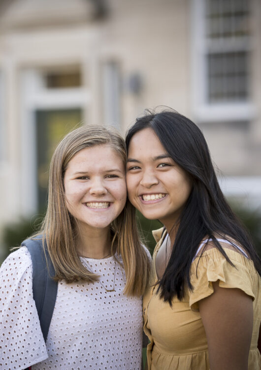 Two girls stand cheek to cheek smiling