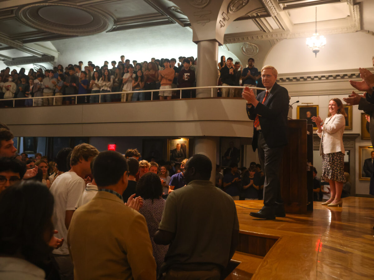 Principal Rawson stands on Assembly Hall stage clapping surrounded by an Assembly Hall full of students