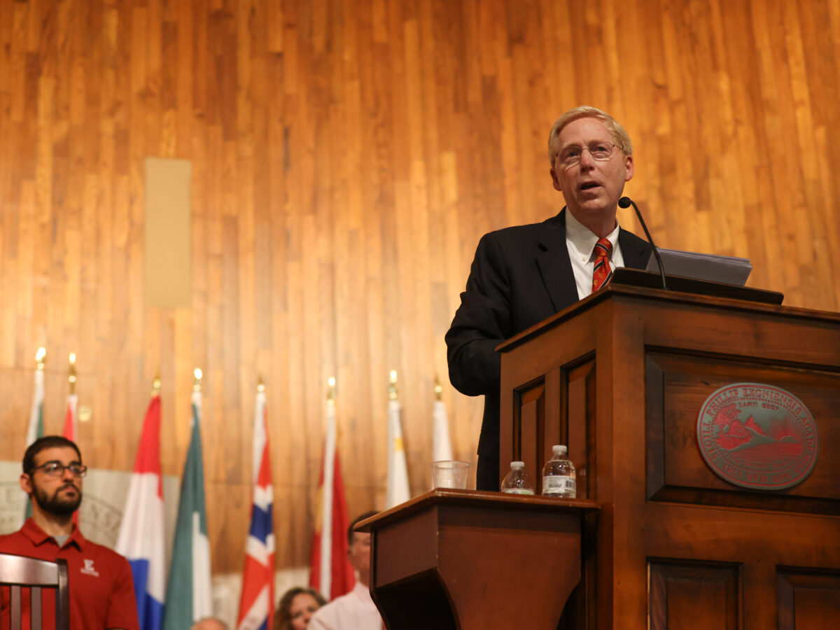 Principal Rawson stands at podium on Assembly Hall stage