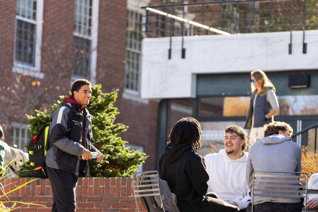 Student walks by and talks to group of students sitting on campus.