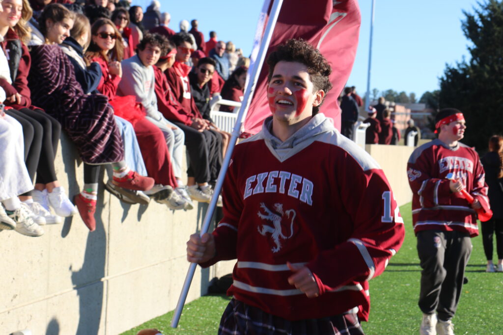 Boy runs through the crowd at E/A weekend while holding an Exeter flag and wearing an Exeter jersey.