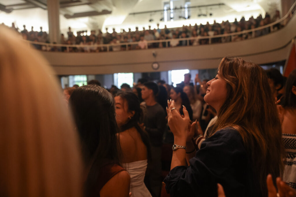 Girl standing in Assembly Hall while clapping and watching the assembly speaker.