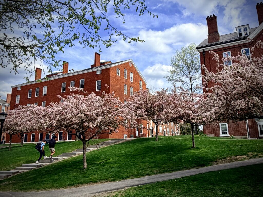Two students walk the stairs to Soule Hall, and Abbott Hall framed by pink and white blossoms on Exeter's campus.