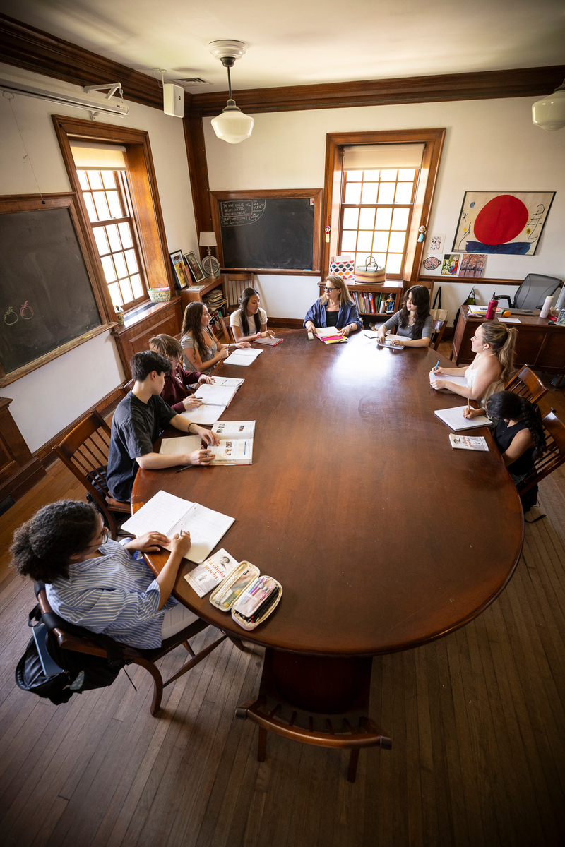 students sit at an oval Harkness table in a classroom
