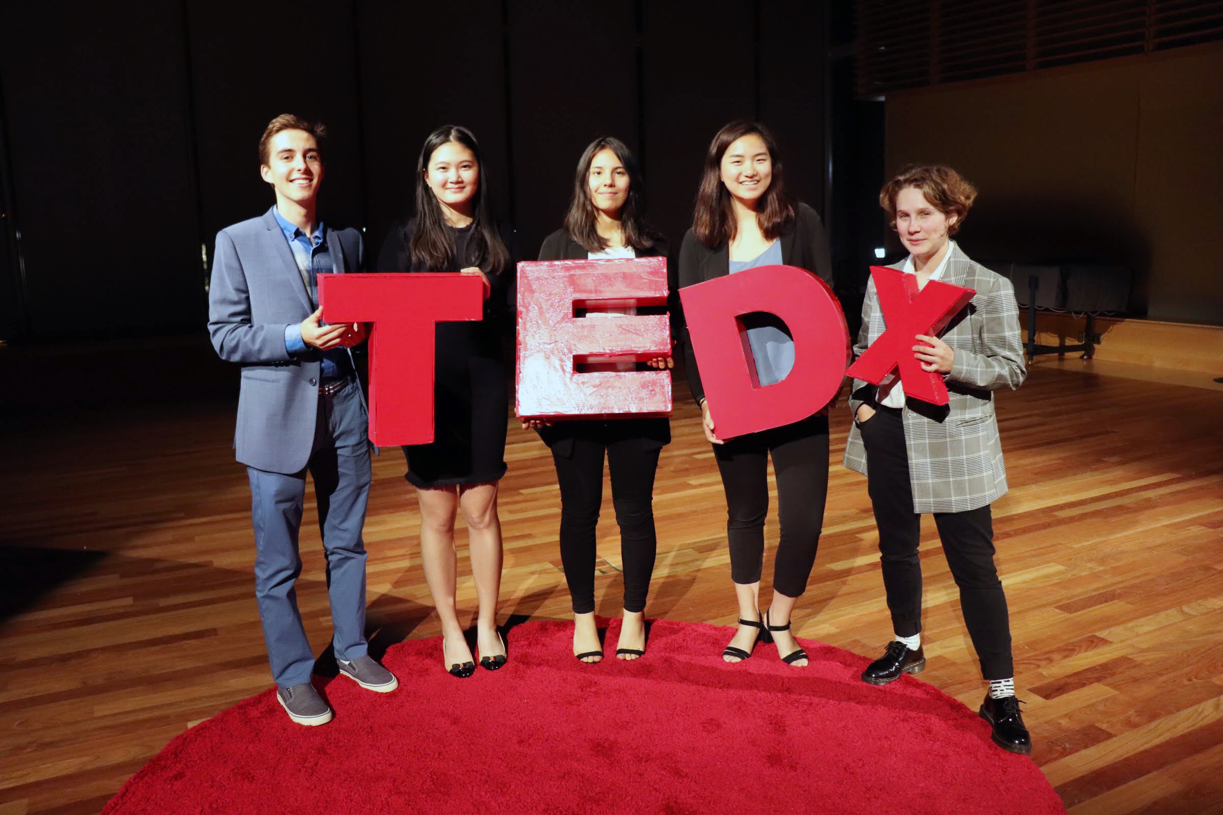 Exeter students stand with the logo TEDx in large, wooden letters.