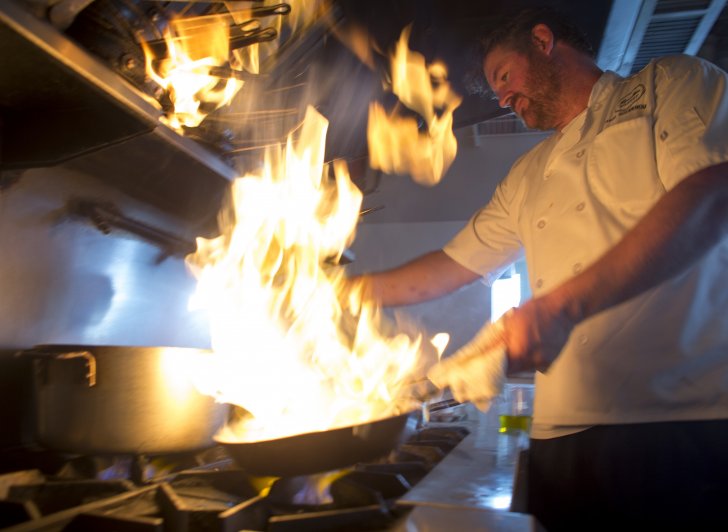 Chef Jason Goodenough working at a stove with flaming food.  