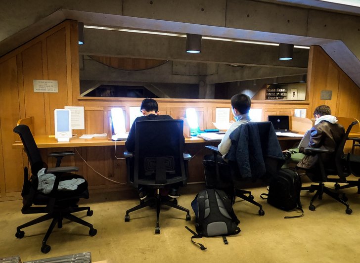 Three students sit in front of light therapy lamps in the Academy Library.