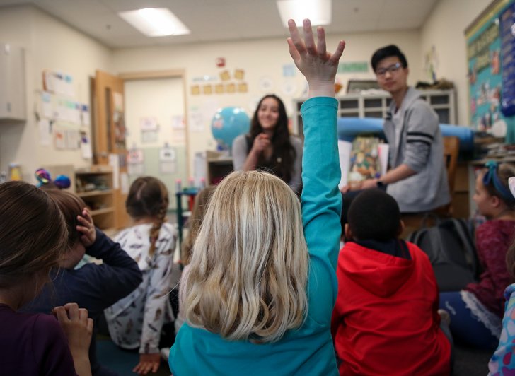 A second-grader at Main Street School raises her hand to ask a question during story time with Phillips Exeter Academy students. 