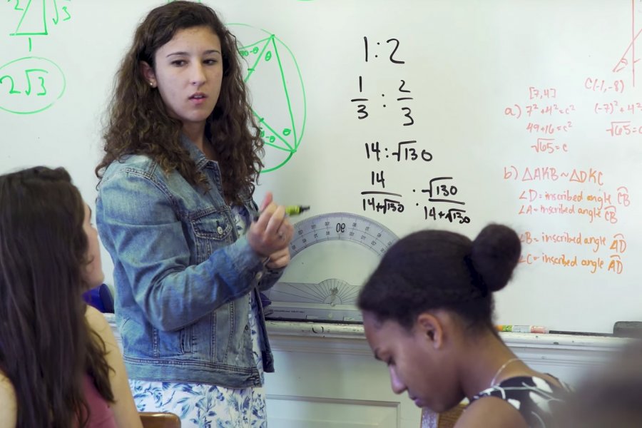 Student standing at the board presenting a math problem to students seated at the Harkness table.