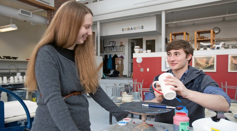Carla Collins smiles as a student as he applies glaze to a ceramic mug
