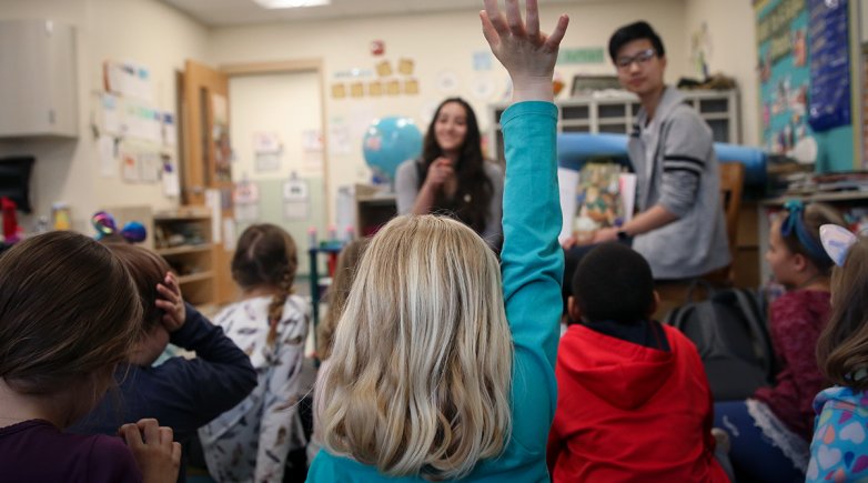A second-grader at Main Street School raises her hand to ask a question during story time with Phillips Exeter Academy students. 